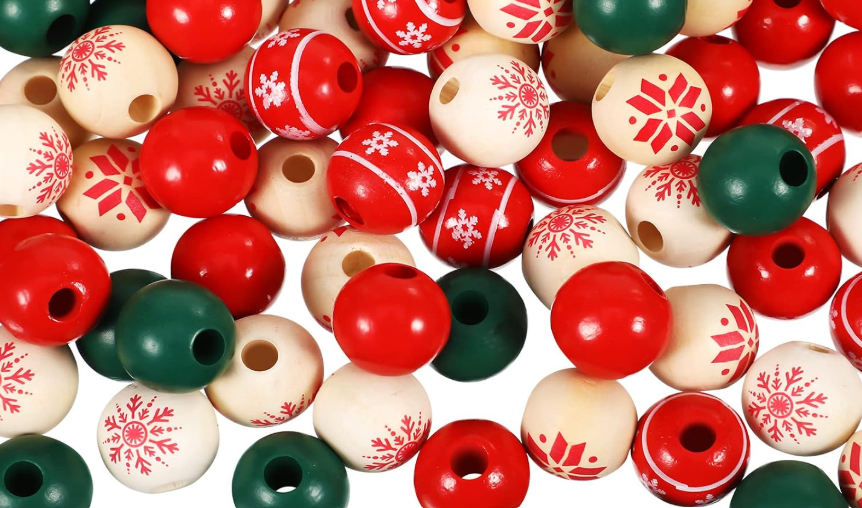 A pile of round wooden beads in red, dark green, and natural cream, decorated with red snowflake and geometric patterns, on a white background.