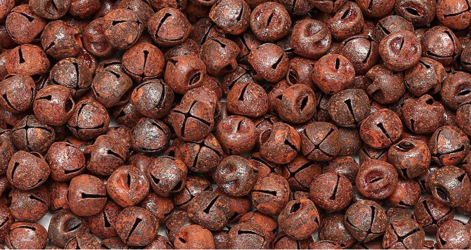 A dense pile of small round brown bells with cutout tops, filling the frame against a white background at the edges.